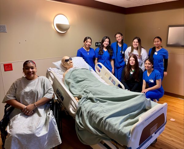 Students pose with a mannequin in the  hospital room. *In wheelchair: Tinia Boyd *Standing (Left-right): Kenia Castaneda-Benavides, Penelope Macias-Garcia, Peyten Turley (N. Boone HS), Alexa Pollace (N. Boone HS), Rose Mary *Bottom row (Left-right): Kamryn Stout (Jefferson HS), Yaritza Ramoz-Diaz (Jefferson HS)